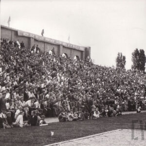 tłum ludzi siedzący na trybunie przy boisku piłkarskim
