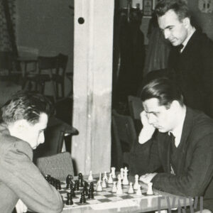 grupa elegancko ubranych mężczyzn siedząca przy stole i pochylona nad szachownicą