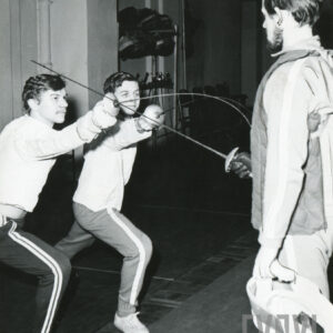 dwaj młodzi mężczyźni ćwiczących pchnięcie na trzecim mężczyźnie ubranym w kamizelkę ochronną