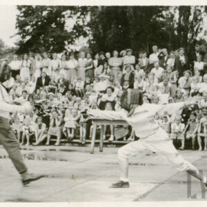 dwie osoby w strojach szermierczych walczące na planszy otoczonej widzami