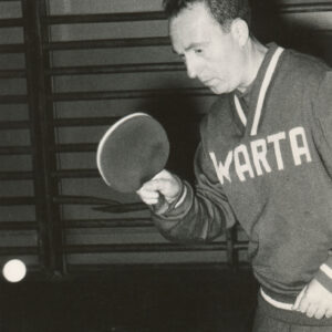 mężczyzna w średnim wieku, w klubowym dresie sportowym przygotowujący się do uderzenia rakietką nadlatującej piłki