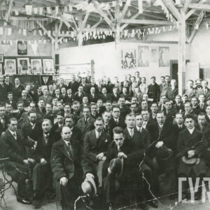 duża grupa mężczyzn w garniturach i płaszczach siedzących na krzesełkach w hali