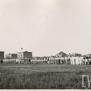 duża grupa osób w strojach sportowych stojących na boisku, w tle budynki mieszkalne z cegły