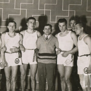 grupa młodych mężczyzn w strojach sportowych i stojący pośrodku mężczyzna w średnim wieku ubrany w elegancki strój 