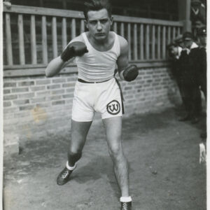 młody mężczyzna w stroju sportowym z rękawicami bokserskimi na dłoniach, pozujący do fotografii w pozycji bokserskiej, na tle ceglanego murku z drewnianą balustradą