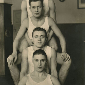 czterech mężczyzn w białych podkoszulkach, siedzących w rzędzie jeden z drugim