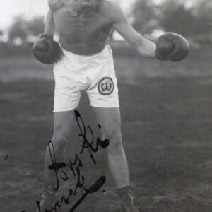 młody mężczyzna w stroju sportowym z rękawicami bokserskimi na dłoniach pozujący do fotografii w pozycji bokserskiej, stoi na trawie