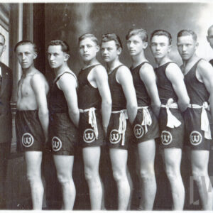 jeden mężczyzna w średnim wieku ubrany w garnitur i grupa młodych mężczyzn stojących w rzędzie w strojach sportowych