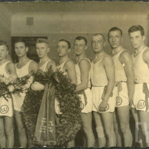 grupa młodych mężczyzn w strojach sportowych i stojący pierwszy od lewej mężczyzna w średnim wieku ubrany w elegancki strój 