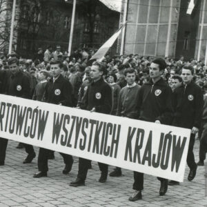 grupa młodych mężczyzn w strojach klubowych maszerująca ulicą, mężczyźni w pierwszym rzędzie trzymają transparent propagandowy