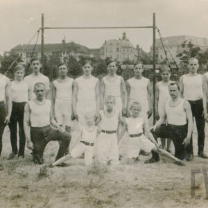 trzech chłopców i grupa mężczyzn w różnym wieku, ubranych w stroje sportowe, pozujących placu z rzadka porośniętym trawą