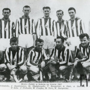 grupa mężczyzn w strojach sportowych stojących i kucających w dwóch rzędach, wszyscy trzymają w dłoniach laski hokejowe, a jeden z nich nosi dodatkowe ochraniacze na nogach