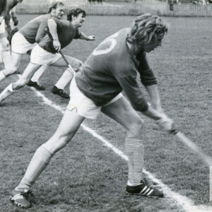 mężczyźni w strojach sportowych, trzymający laski hokejowe, ćwiczący na trawiastym boisku