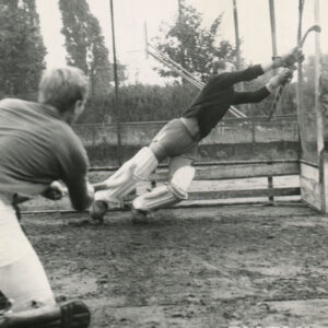 dwóch mężczyzn w strojach sportowych, laskami hokejowymi w głowach, trenujący na błotnistym boisku