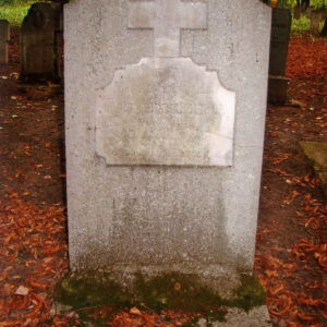 kamienna płyta nagrobna z wtopioną tablicą epitafijną i krzyżem łacińskim; na nią inne nagrobki, pnie drzew i teren pokryty suchymi liśćmi