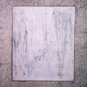 biała, prostokątna tablica z zatartymi napisami wtopiona w płytę nagrobną 
