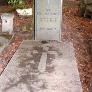 leżąca, kamienna płyta z krzyżem łacińskim i wysoka stela z czarnymi napisami i krzyżem łacińskim w górnej części; z tyłu inne nagrobki i drzewa 