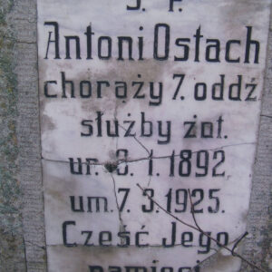 biała, prostokątna tablica z pęknięciami wtopiona w płytę nagrobną, na niej czarne napisy
