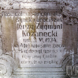 biała tablica z wyrytymi napisami wtopiona w płytę nagrobną