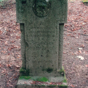 zabrudzona płyta nagrobna z krzyżem, na którym znajdują się napisy oraz medalion ze śladami płaskorzeźby