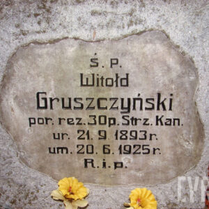kamienna tablica o nieregularnym kształcie z czarnymi napisami wtopiona w płytę nagrobną