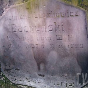 zabrudzona tablica o nieregularnym kształcie z wyrytymi napisami wtopiona w płytę nagrobną