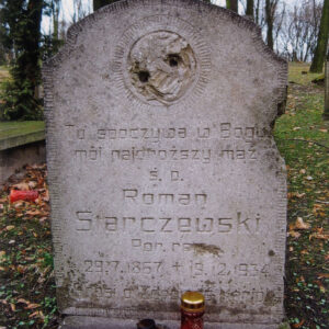 płyta nagrobna obramowana żłobieniami z inskrypcją i śladem po tondzie, za nią teren cmentarza z wysokimi drzewami