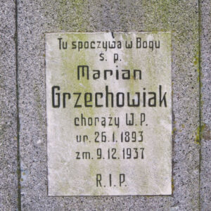 biała, prostokątna tablica z czarnymi napisami wtopiona w płytę nagrobną