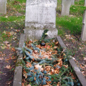 obmurowany grób, wewnątrz którego poukładano gałązki świerku, stela z pozostałością krzyża i inskrypcją