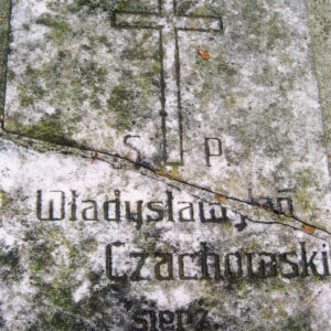 zabrudzona prostokątna tablica z poziomym pęknięciem, napisami i krzyżem łacińskim wtopiona w płytę nagrobną