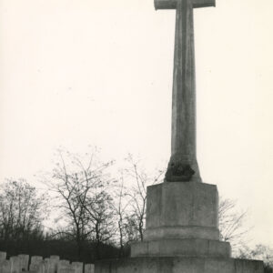 Wysoki, kamienny krzyż na postumencie. Przy nim jednakowe pionowe płyty nagrobne, a za nimi drzewa bez liści.