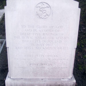 Biały, kamienna płyta nagrobna na niskim cokole z inskrypcją. Za nią fragmenty nagrobków.