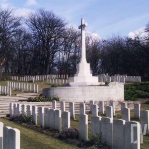 Liczne nagrobki o jednolitym wyglądzie. Pośrodku wysoki krzyż na postumencie. Z tyłu drzewa bez liści.