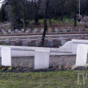 rząd białych płyt nagrobnych stojących wśród drzew, za nimi murek, dalej w głębi kilka rzędów nagrobków w formie krzyży