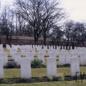 Kilka rzędów nagrobków o jednolitym wyglądzie, na terenie porośniętym trawą. Za nimi drzewa i mur Małej Śluzy.