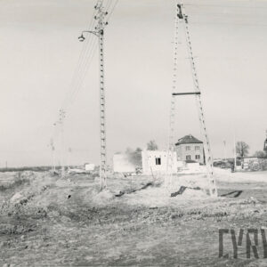 piaszczysta, nieutwardzona droga, wzdłuż której stoją lamy uliczne, obok nich budynek z cegły