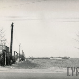 domy z cegieł stojące przy ubitej, piaszczystej drodze; po jednej stronie drogi stoją domy i słupy energetyczne, po drugiej stronie widoczne pola 