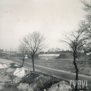 skrzyżowanie dwóch ulic, obok których stoi usytuowana w nasypie ziemnym budowla z cegieł; widoczne drzewa oraz jadący po drodze samochód, w głębi domy z cegieł 