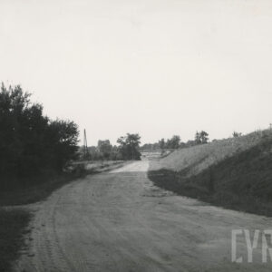 polna droga otoczona z jednej strony wałem ziemny, z drugiej drzewami i trawą, w oddali widać ulokowaną w nasypie budowlę z cegieł