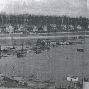 rzeka z zabudowaniami i pływającymi po niej statkami, w głębi domy wzdłuż brukowanej, nadbrzeżnej ulicy