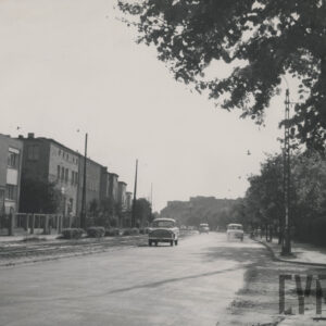 szeroka droga ciągnąca się równolegle do torów tramwajowych, na której widać jadące samochody, po jednej stronie ulicy drzewa, po drugiej domy mieszkalne 