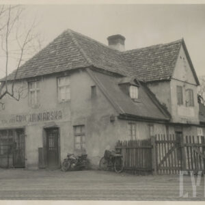 murowany dom z cegieł, pokryty dachówką, otoczony płotem; budynek stoi przy utwardzanej, brukowanej drodze