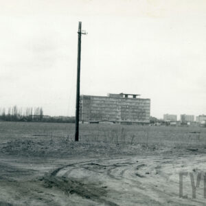 kilkupiętrowy budynek mieszkalny, stojący na pustym, z rzadka porośniętym trawą placu, w oddali widoczne 