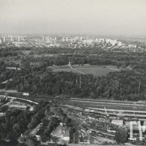 duży teren parkowy leżący przy ulicy i torach kolejowych, widoczne za nim osiedle bloków z wielkiej płyty