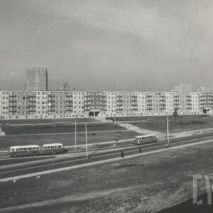 ulica, po której przemieszczają się autobusy, wzdłuż drogi rozciąga się blok mieszkalny z wielkiej płyty