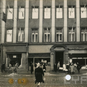 fragment fasady hotelu z wystawami sklepów, przed budynkiem idący ludzie w zimowych strojach