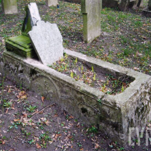 wysokie, zdobione obmurowanie mogiły ziemnej, wewnątrz umieszczona uszkodzona tablica z napisami, wokół teren cmentarza i inne nagrobki