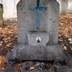 kamienna płyta na cokole, pośrodku niej czary krzyż łaciński, a w dolnej części owalny medalion portretowy, wewnątrz obmurowania stoi kamienny pojemnik na rośliny wokół teren cmentarza