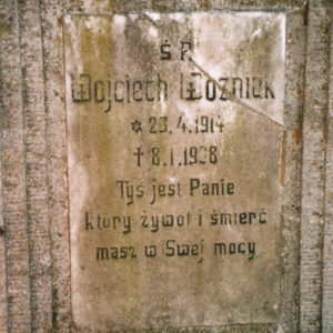 prostokątna, zabrudzona tablica pęknięta ukośnie, z wyrytymi napisami, wtopiona w płytę nagrobną