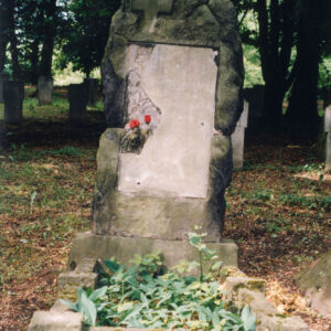 obmurowana mogiła ziemna i masywna płyta nagrobna złożona z dwóch bloków piaskowca, na niej uszkodzona tablica epitafijna, wokół teren cmentarza, inne nagrobki i drzewa